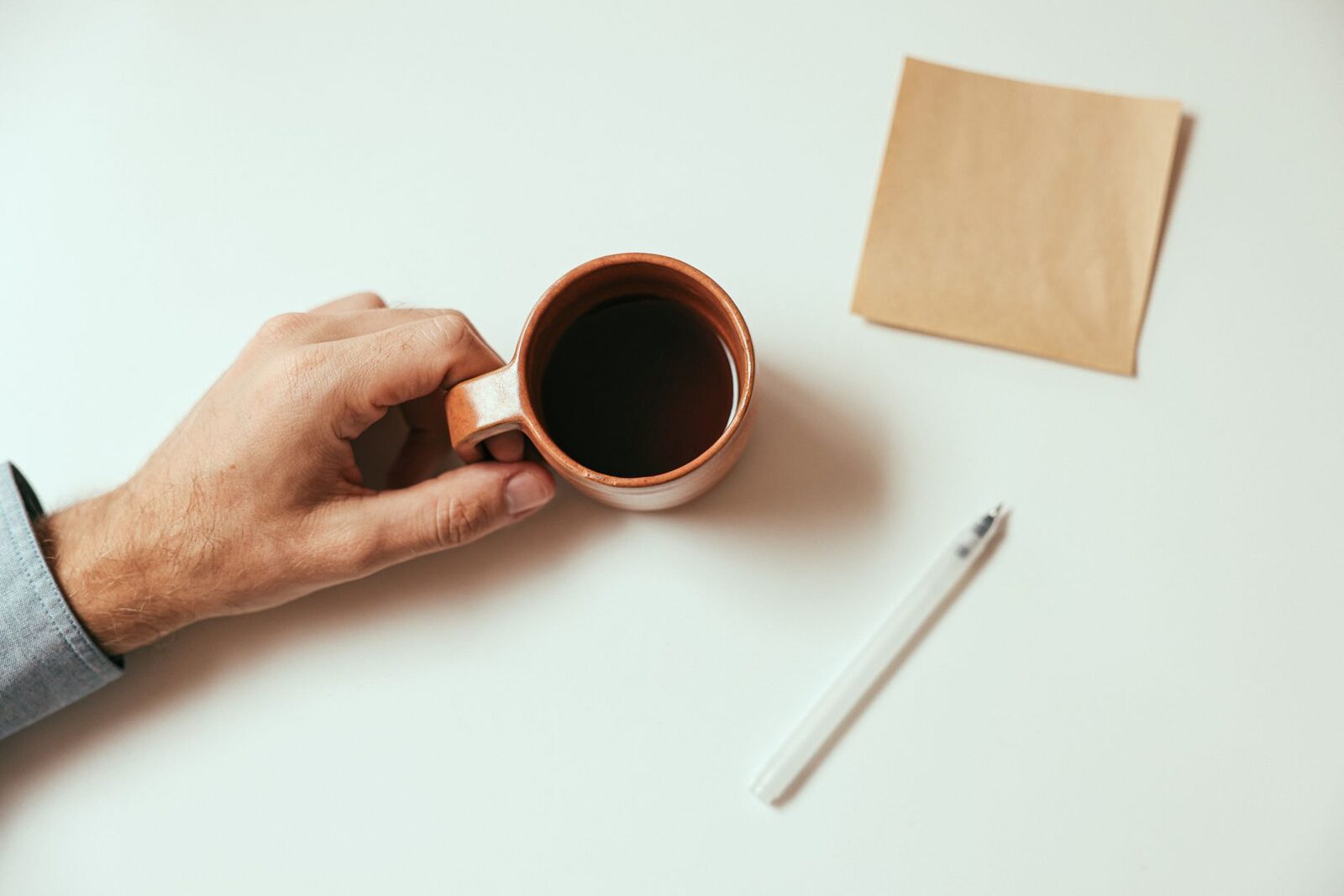 A hand holding a coffee mug on a desk with a pen and paper, creating a minimalist vibe.