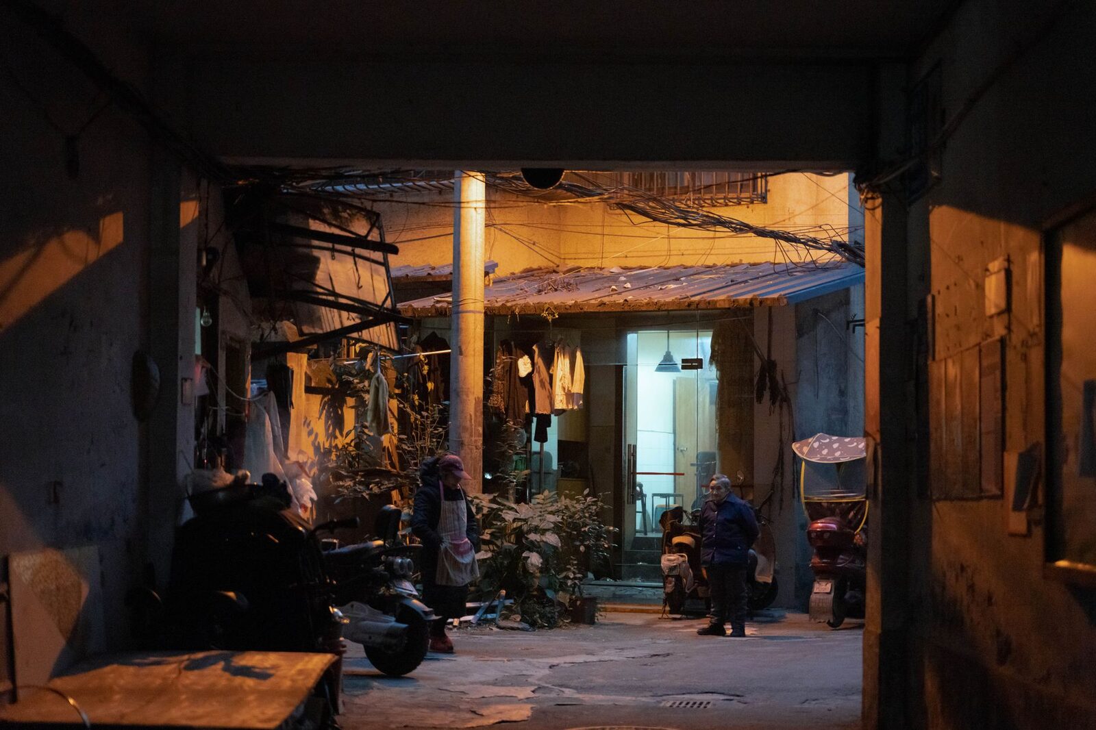 Two people conversing in a dimly lit urban alleyway during evening hours.