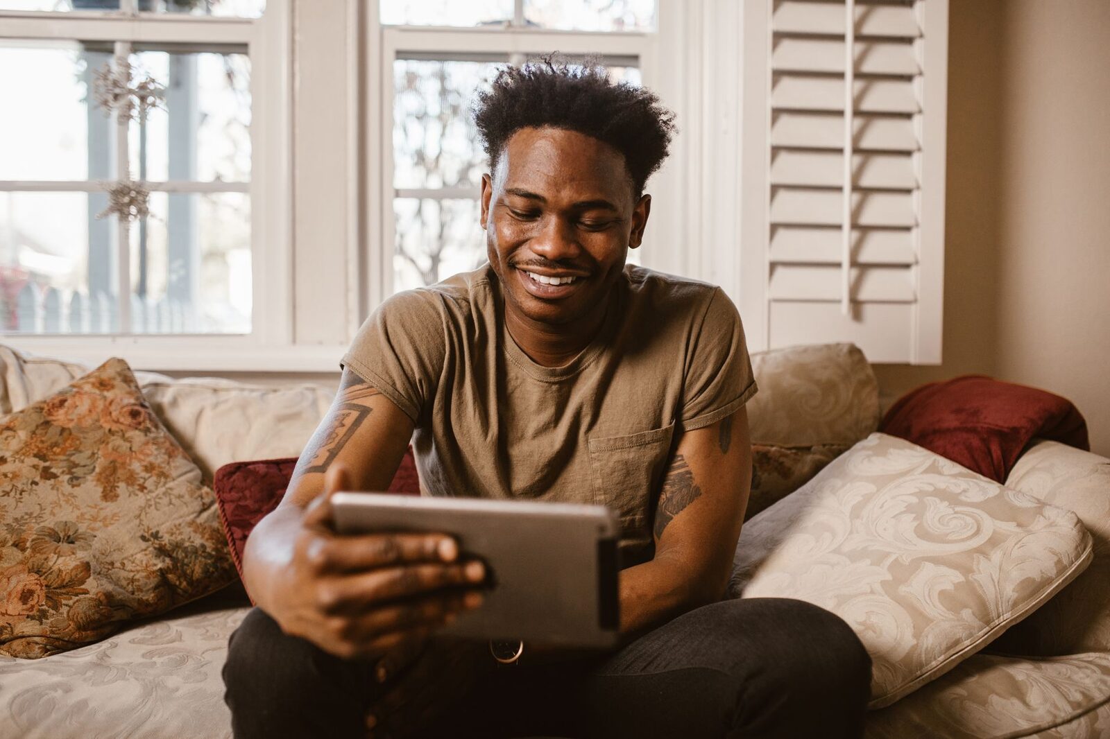 A happy man uses a tablet for a video call while sitting comfortably on his couch at home.