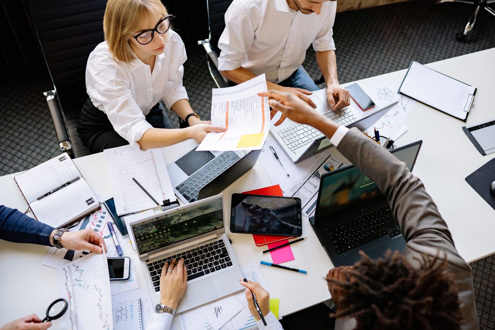 Diverse team collaborating in a modern office with laptops and documents.